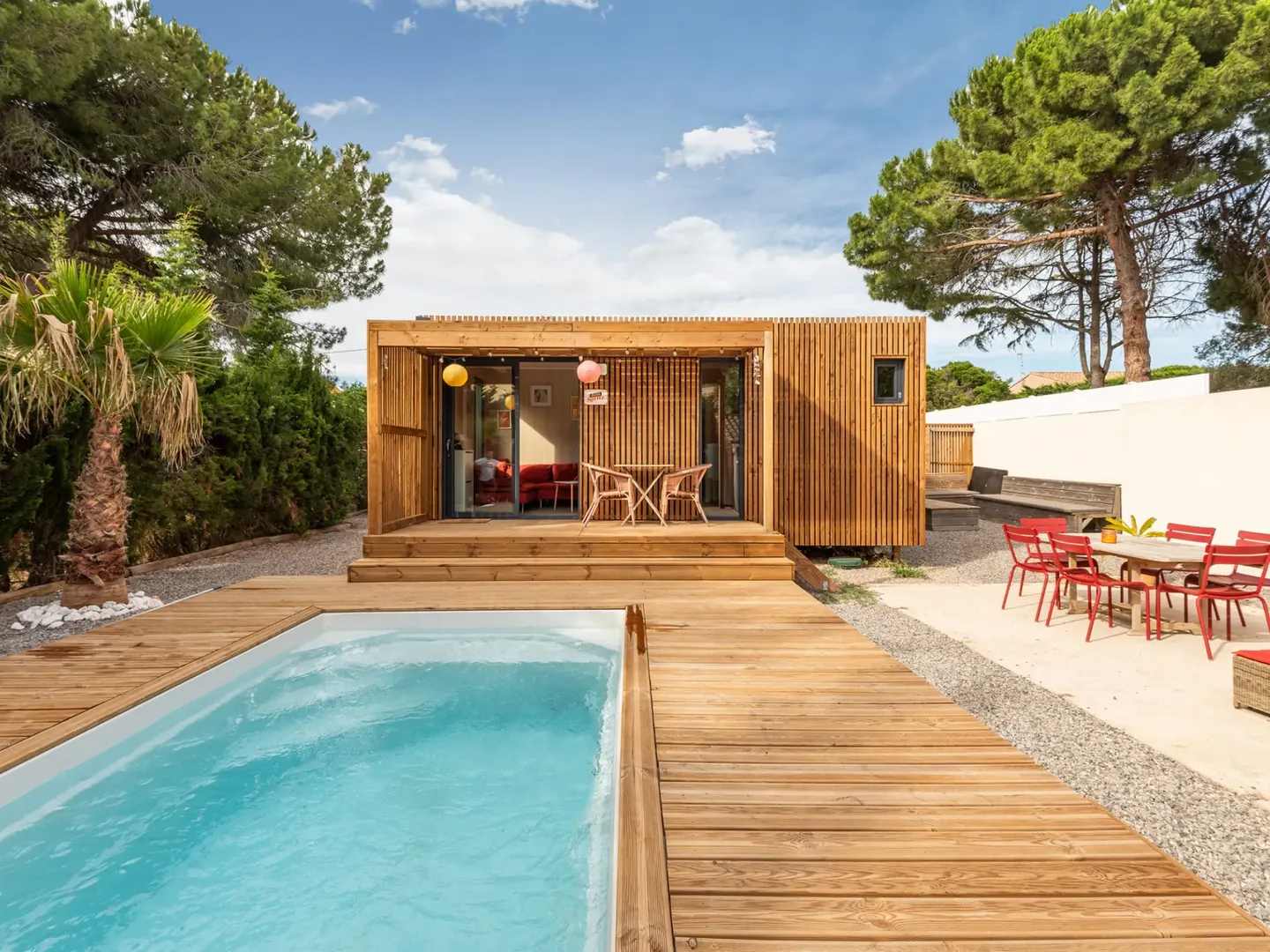 Studio de jardin Greenkub GK40 en ossature bois ouvert sur une terrasse en bois bordant une piscine, sous les pins parasols